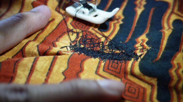 Close up of electric sewing machine foot stitching traditional batik patterned fabric with black thread