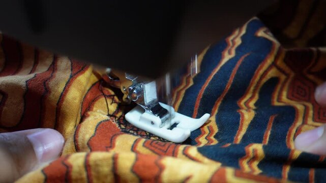 Close up of electric sewing machine foot stitching traditional batik patterned fabric with black thread