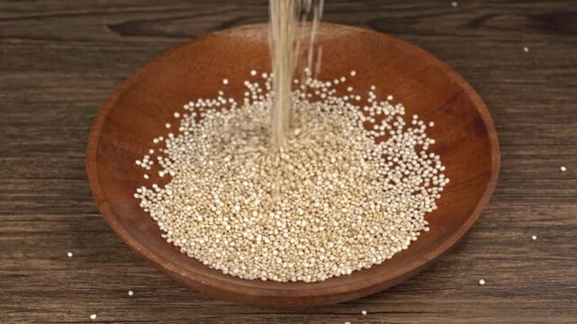 Pouring raw white quinoa seeds into a wooden bowl