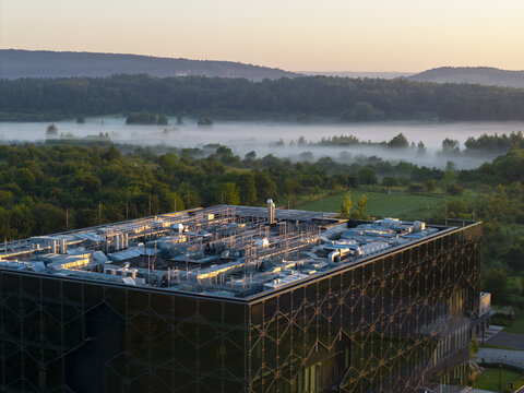 Aerial view of an AI data center with rooftop cooling systems, surrounded by lush forests and morning mist under a golden sky in Krakow, Lesser Poland Voivode, Poland.