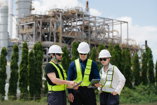 Team of engineers working together at an oil and gas refinery surrounded by heavy industrial machinery and equipment