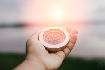 Hand holding compass at sunset symbolizing direction and future journey. © sawitreelyaon