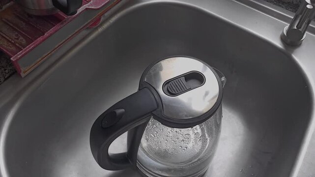 A person places an electric kettle filled with water onto its heating base on a kitchen counter. The scene captures a simple household task related to beverage preparation and daily domestic routines