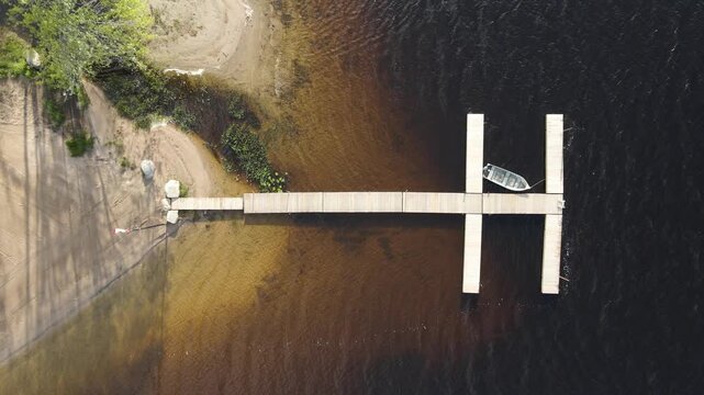 Top down aerial of dock with single boat and shallow lake water at Restoule Ontario, drone ascend
