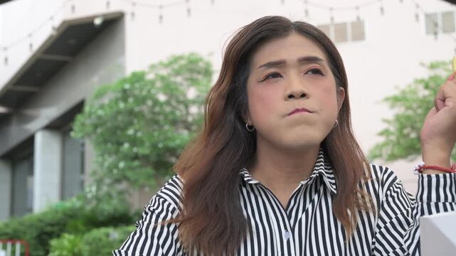 Thai Isan transgender woman in 40s eating French fri outdoors at restaurant. Vertical medium shot portrait of a mature non-binary Southeast Asian trans woman.