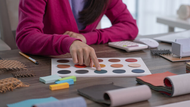 A close up of a designer's finger touching a blue leather swatch on a color palette board surrounded by fabric rolls and wooden blocks.