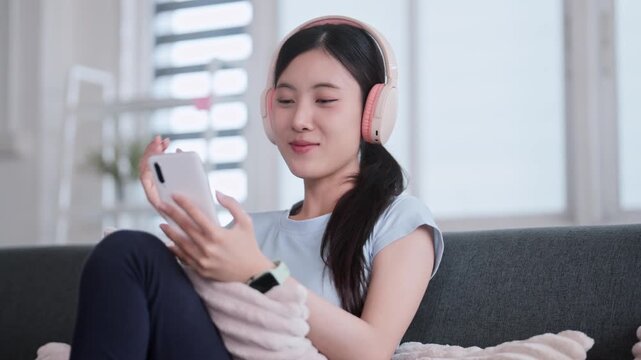 Asian woman in sports attire using phone and headphones indoors