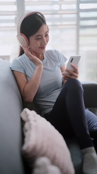 Asian woman in sports attire using phone and headphones indoors