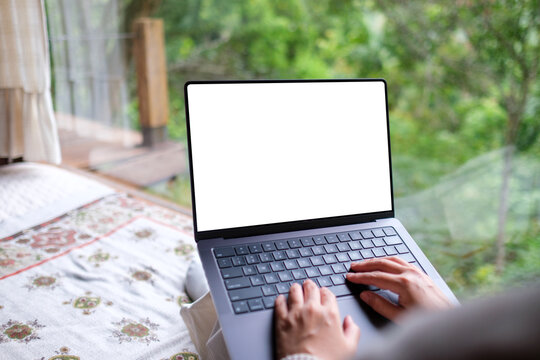 Mockup image of a woman working and typing on laptop computer with blank desktop white screen on the bed at home