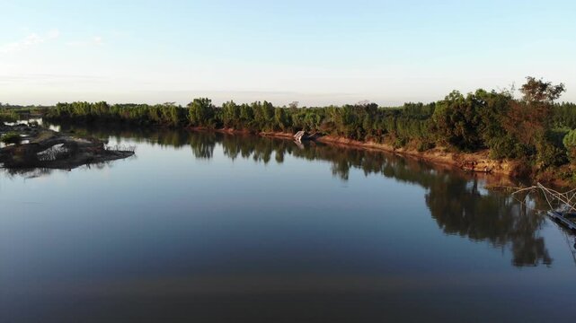 Aerial view of tropical river delta at sunset. Sunlight reflects in calm waters of river. Green forest and trees surround the watercourse at beautiful evening.