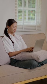 Woman works or chats online on laptop while sitting relaxed on living room sofa