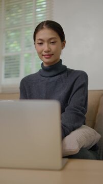 Woman relaxes on sofa in cozy living room using laptop