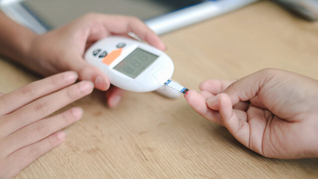 Close-up of a blood glucose meter testing blood sugar from a fingertip, representing diabetes monitoring, home healthcare, and wellness.