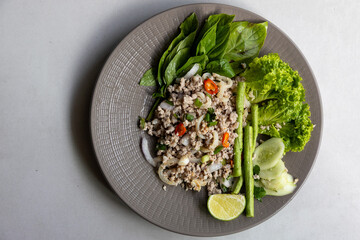 Thai food, spicy minced pork salad Larb Moo with vegetables on grey plate on grey background, close up. Top view. © Lyudmila