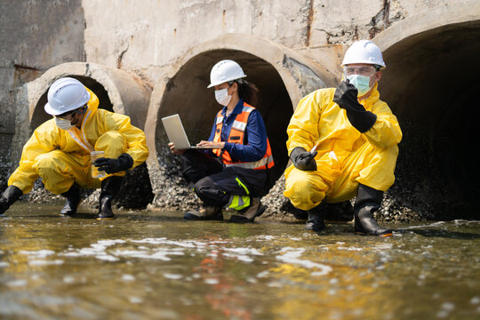 Serious team of worker and engineer in yellow protective suit conducting wastewater inspection. Focused professionals perform water pollution analysis inside an industrial sewer