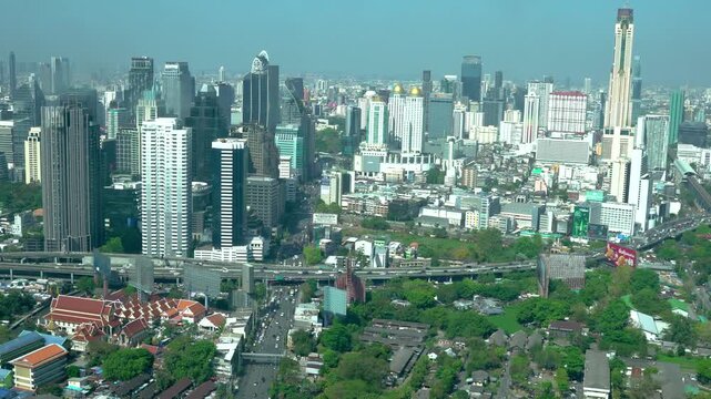Static wide view of the city skyline featuring high-rise towers, elevated expressways, a temple and dense urban neighborhoods under a hazy sky.