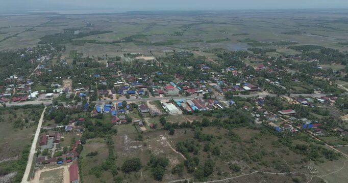 Aerial view: a sprawling rural community of scattered houses and lush vegetation spreads across a vast, flat landscape, bisected by a main road.