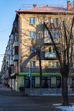 Yaroslavl, Russia - February 22, 2025: Corner residential building with green ground-floor cafe, bare trees, blue sky, and crosswalk on street