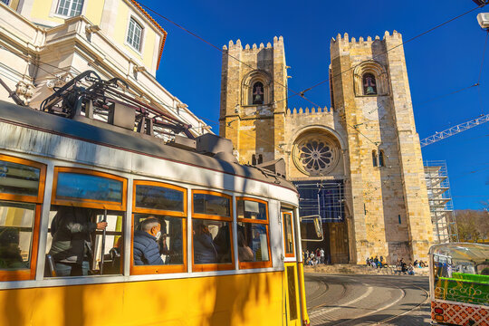 A traditional yellow vintage tram ascends a steep, narrow cobblestone street lined with historic buildings in Lisbon