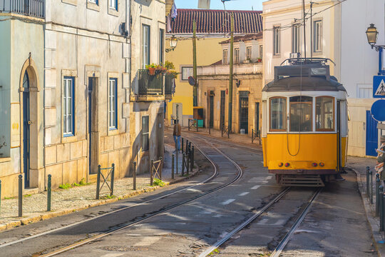 A traditional yellow vintage tram ascends a steep, narrow cobblestone street lined with historic buildings in Lisbon
