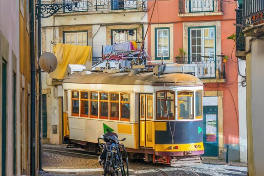 A traditional yellow vintage tram ascends a steep, narrow cobblestone street lined with historic buildings in Lisbon