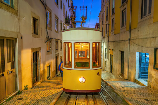 A classic yellow funicular tram ascending a steep, narrow cobblestone street lined with traditional colorful buildings  in Lisbon