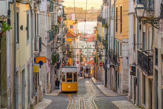 A classic yellow funicular tram ascending a steep, narrow cobblestone street lined with traditional colorful buildings  in Lisbon