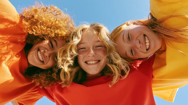 Group of happy diverse friends looking down into the camera, smiling faces against a bright blue sky, low angle perspective