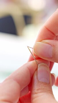 Seamstress hands threading a sewing needle