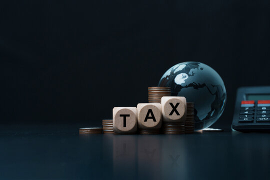 Global tax planning concept. Wooden blocks spelling TAX on stacked coins with a glass globe and calculator on a dark background. Corporate tax, financial management, economy, accounting.