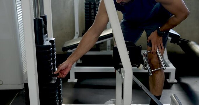 Young Asian man adjusts weight stack pin on cable machine in modern gym, setting resistance before strength workout, solo fitness preparation, arm training routine, wellness, healthy lifestyle.