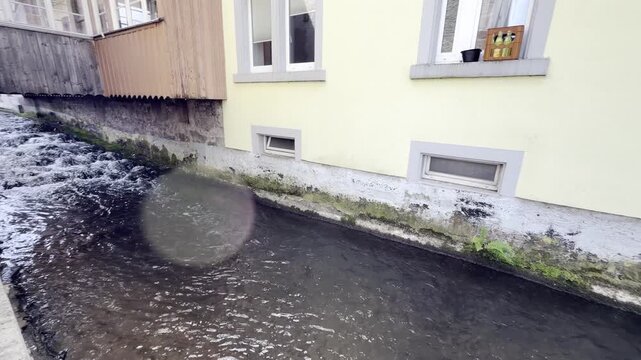In H&ouml;llstein, Germany, a stream channeled by stone walls flows past houses whose facades are covered with moss, panning shot