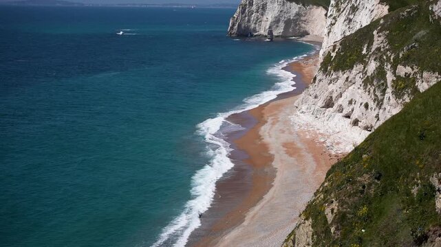 Waves crashing against the beach of the Jurassic coast, with white cliffs outlining the coastline