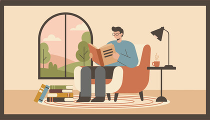 Fototapeta premium Man wearing glasses sitting in a comfortable armchair and reading a book in his cozy living room at sunset.