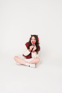 A pretty girl in a burgundy sweater with bows in her hair holds a donut with candles stuck into it in the shape of the number 19. Birthday concept