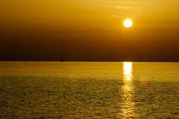 A sailboat and a buoy are visible on the sea during a golden sunset. © Nick