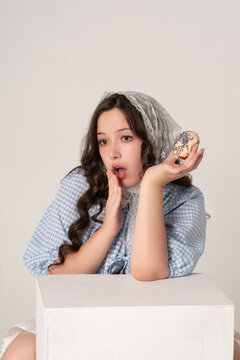 A beautiful girl in a lace headscarf and a blue checkered blouse holds a donut in her hands