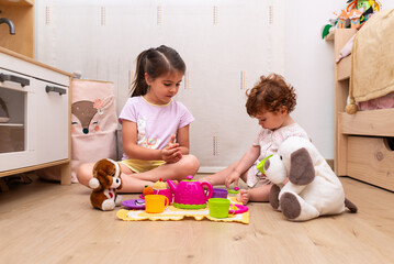 Naklejka premium A 5-year-old girl and her 14-month-old baby sister having a pretend picnic with stuffed animals in their bedroom.