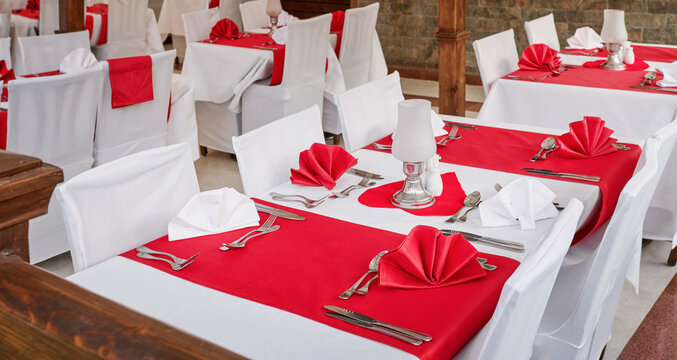 Outdoor restaurant terrace with elegant red and white table setting, folded napkins, silver cutlery, candles and garden view, romantic dining atmosphere for Valentines Day dinner, wedding reception