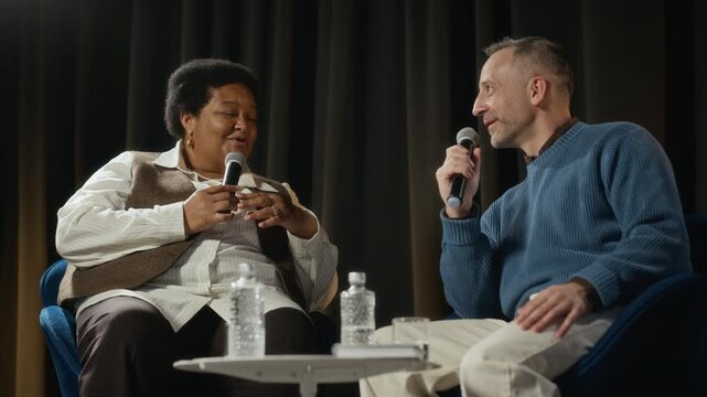 Middle aged Caucasian man and middle aged African American woman speaking during panel discussion. Suitable for corporate communication and educational seminar marketing videos