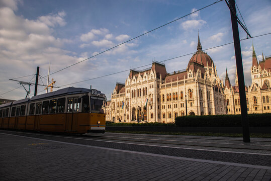 Iconic yellow tram route number 2 passing in front of the Hungarian Parliament Building during golden hour in Budapest
