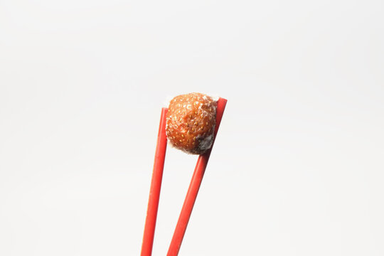 A single rotten strawberry covered in white, fuzzy mold, held up vertically by a pair of red chopsticks against a clean, plain white background.