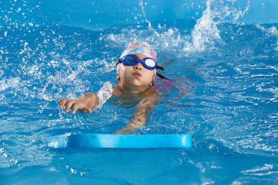Little girl learning to swim in indoor pool with pool board