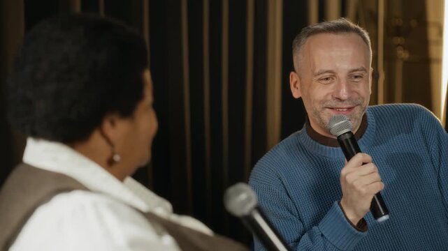 Middle aged Caucasian man and middle aged Black woman holding microphones, speaking during panel discussion. Clip is ideal for corporate communication, diversity training, and event promos