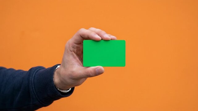 Hand holding a green blank card against an orange background
