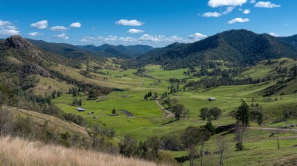 Obraz premium Expansive Green Valley Landscape Surrounded by Rolling Hills and Blue Sky with Fluffy Clouds Under Bright Sunlight