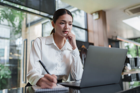 Woman focusing on laptop screen and taking notes in a modern office