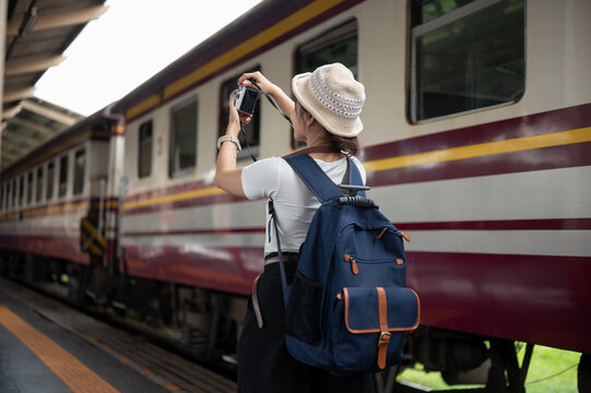 Rear view of woman traveler taking picture of passenger train at railway station platform in daylight