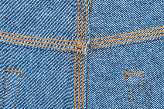 Close up of blue denim fabric with orange stitching and jeans details, three needle job