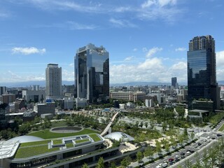 Naklejka premium Panoramic view of modern skyscrapers, urban parkland and cityscape in Osaka, Japan under a clear blue sky.
